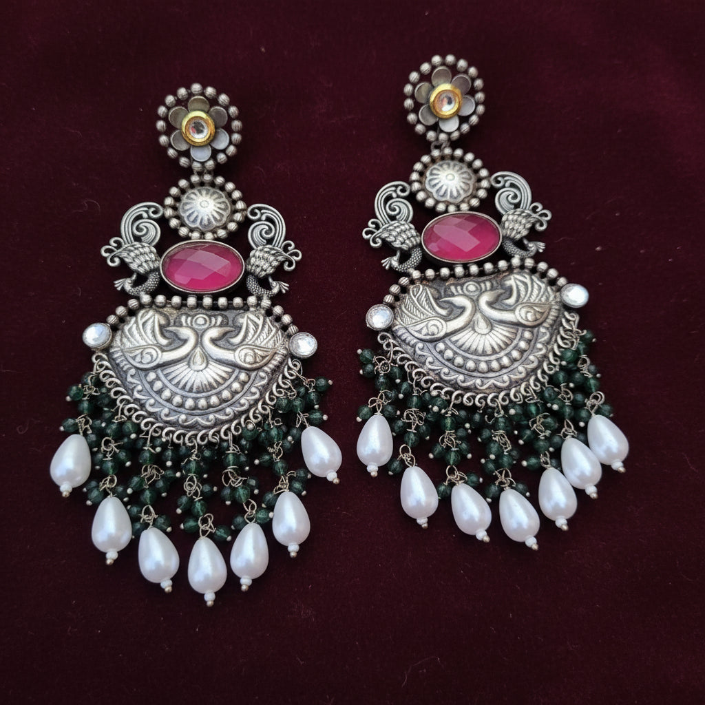 A pair of statement earrings with silver details, pink stones, green bead accents, and white pearl droplets.