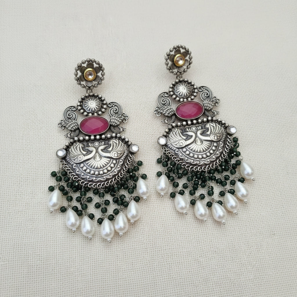 A pair of statement earrings with silver details, pink stones, green bead accents, and white pearl droplets.