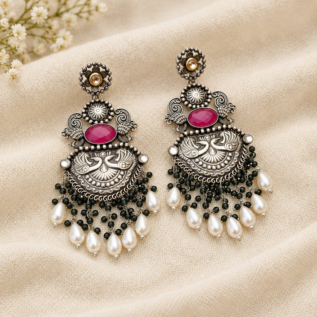 A pair of statement earrings with silver details, pink stones, green bead accents, and white pearl droplets.
