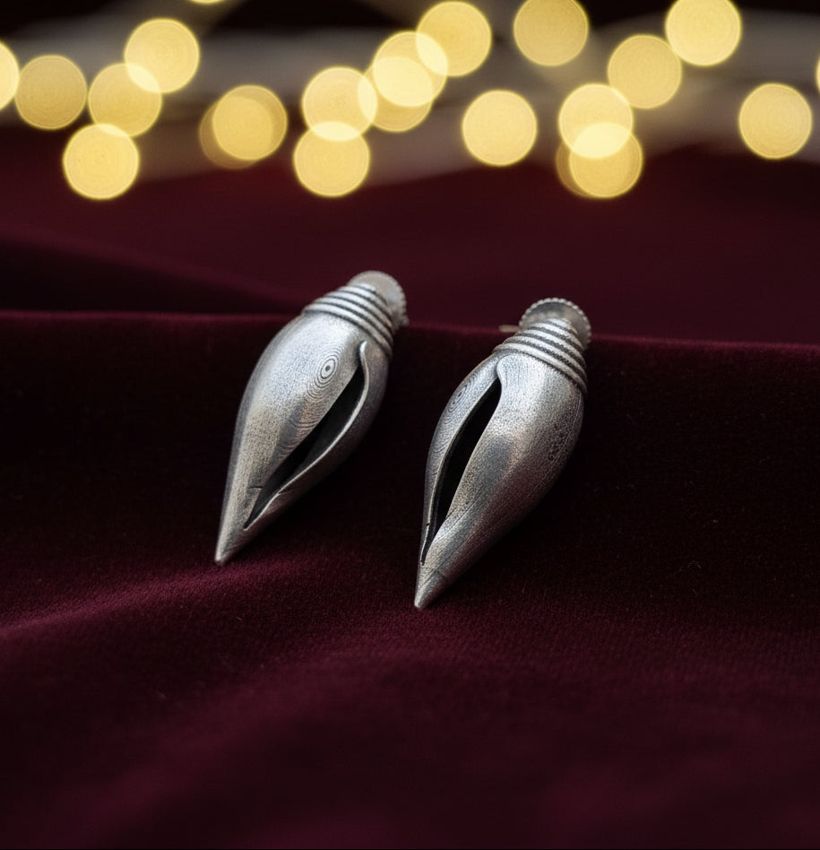This image displays a pair of elegant brass earrings, presented on a textured, gray background that contrasts with the lustrous finish of the earrings. The earrings are designed with a sleek, pointed tip and a smooth, cylindrical body, giving them a modern yet timeless appeal.