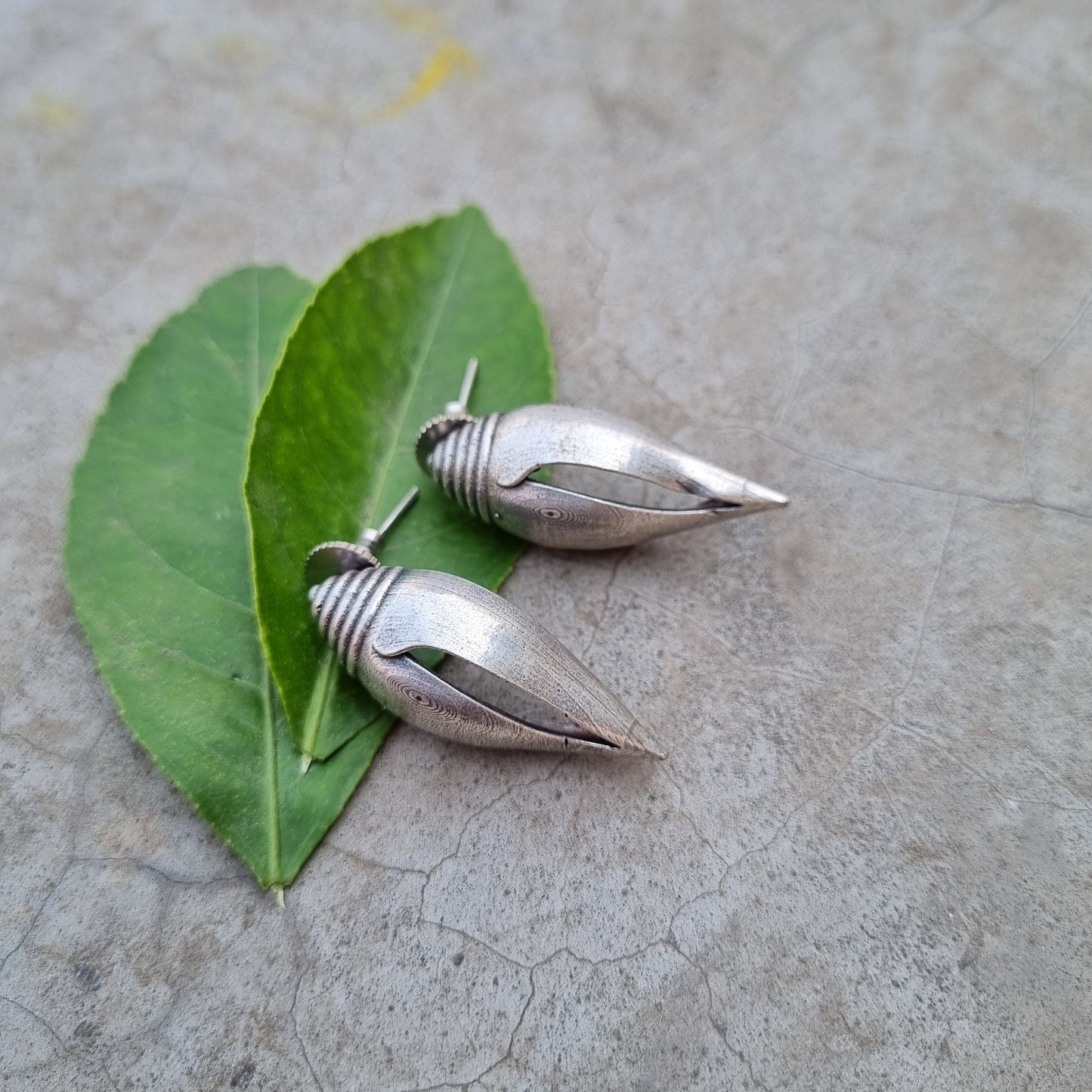 This image displays a pair of elegant brass earrings, presented on a textured, gray background that contrasts with the lustrous finish of the earrings. The earrings are designed with a sleek, pointed tip and a smooth, cylindrical body, giving them a modern yet timeless appeal.