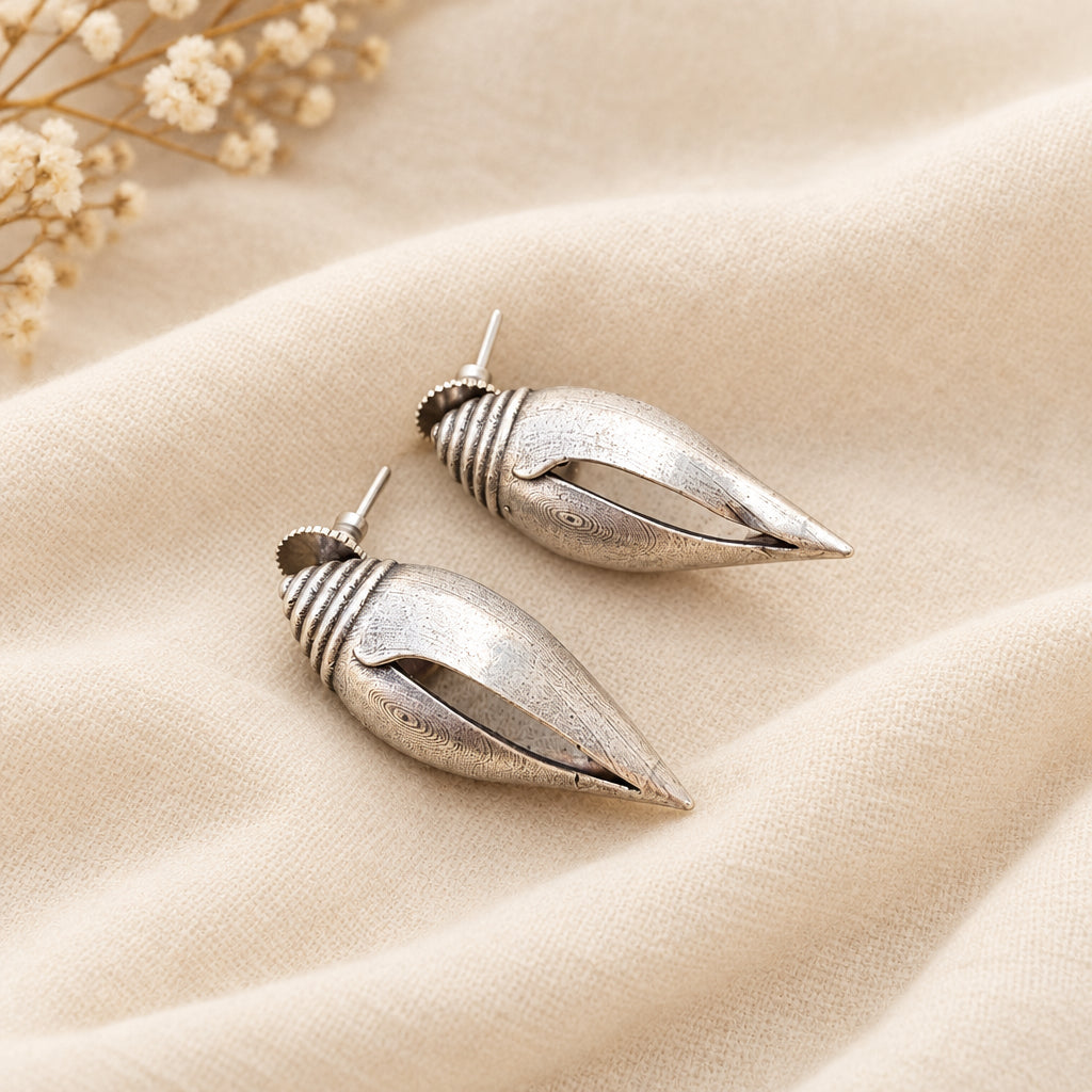 This image displays a pair of elegant brass earrings, presented on a textured, gray background that contrasts with the lustrous finish of the earrings. The earrings are designed with a sleek, pointed tip and a smooth, cylindrical body, giving them a modern yet timeless appeal.
